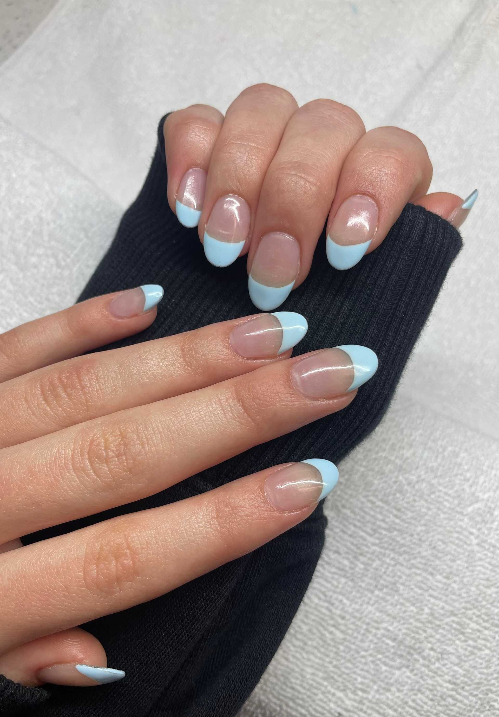 Hands with a blue-green French manicure on short, natural nails over a black sleeve background.