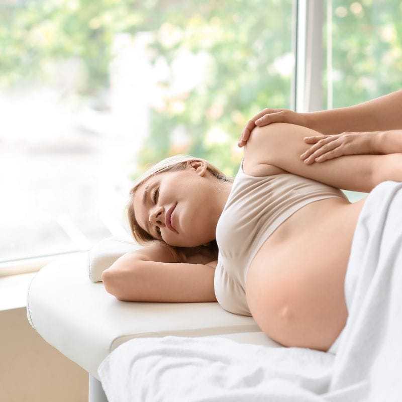 Pregnant woman receiving a relaxing back massage in a bright, soothing environment.