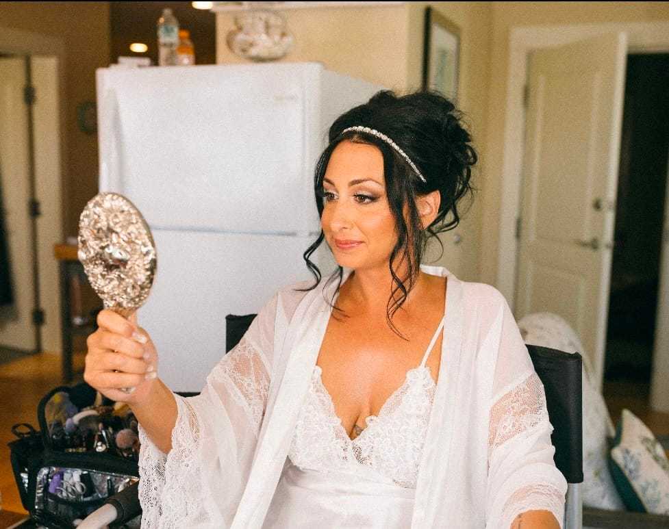Woman in a white robe looking at a handheld mirror, preparing for her wedding day.