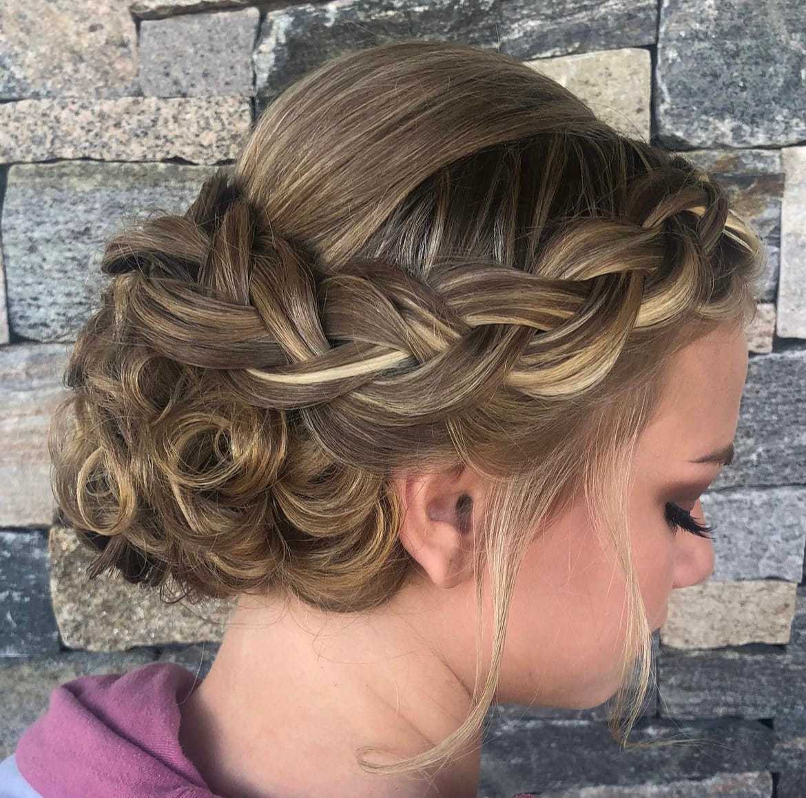Woman with intricate braided updo hairstyle against a stone wall background.
