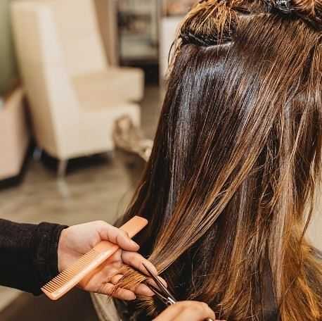 Hairdresser trimming long brown hair in a salon, with a comb in the other hand.