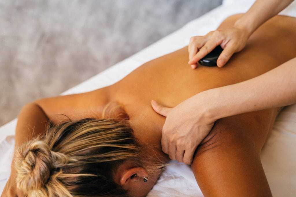 Person receiving a hot stone massage on their back in a relaxing spa setting.