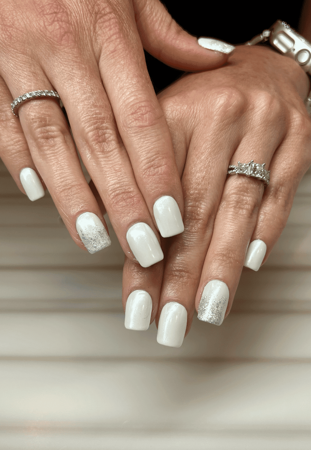 Elegant white nails with silver shimmer designs on a marble background.