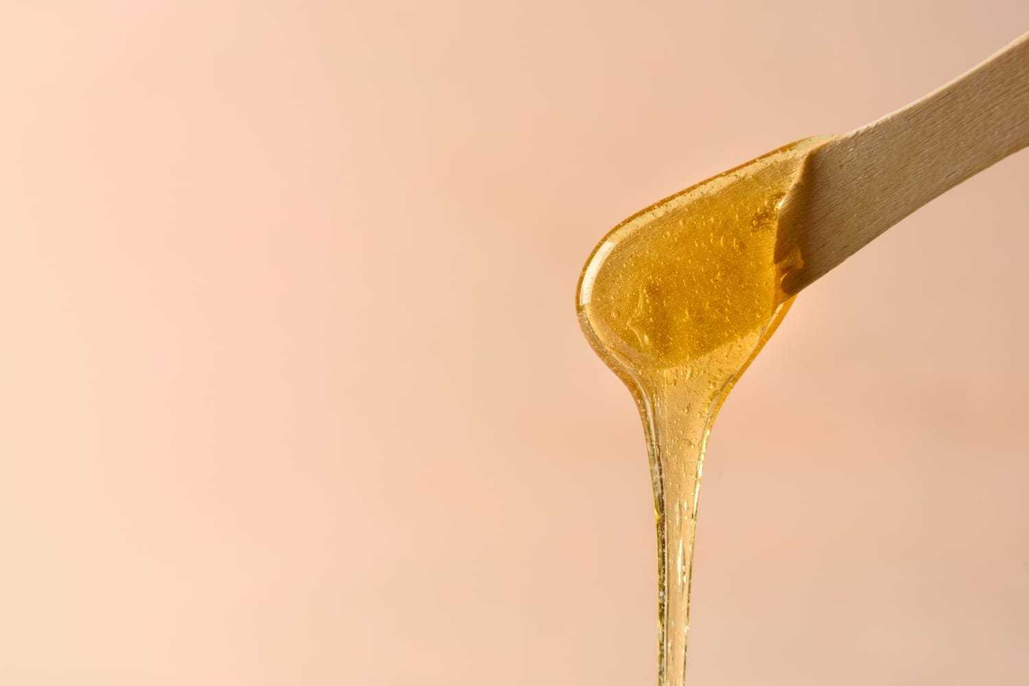 Golden honey dripping from a wooden stick against a light beige background.
