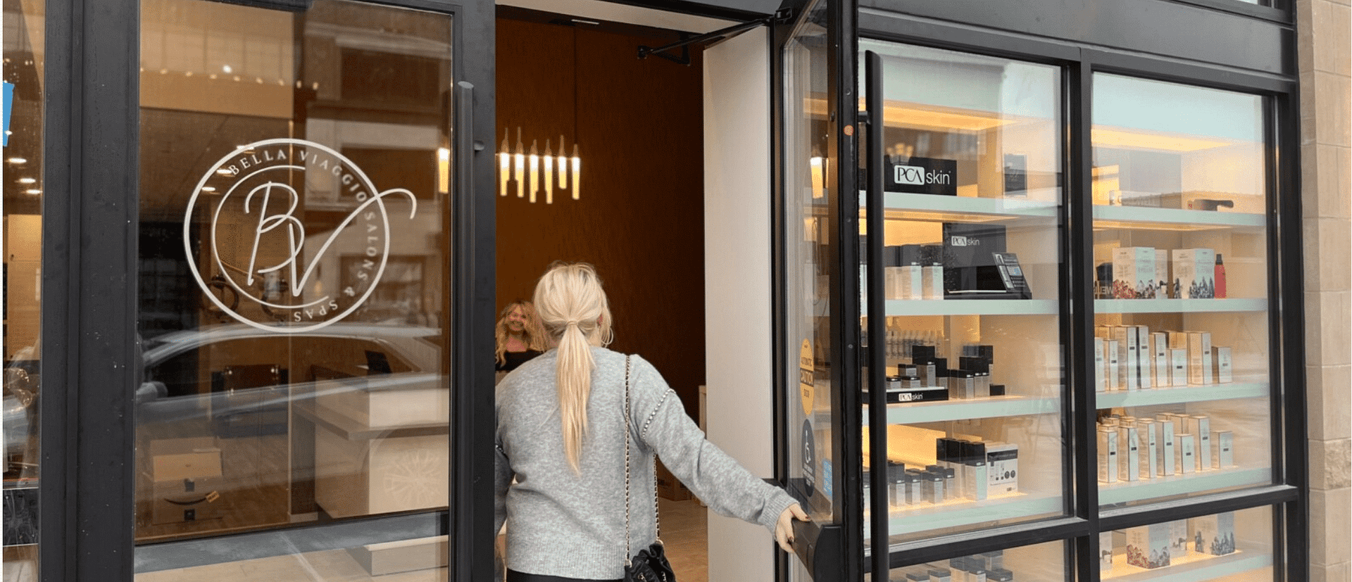 Person entering a beauty spa with products displayed on shelves through a glass door.