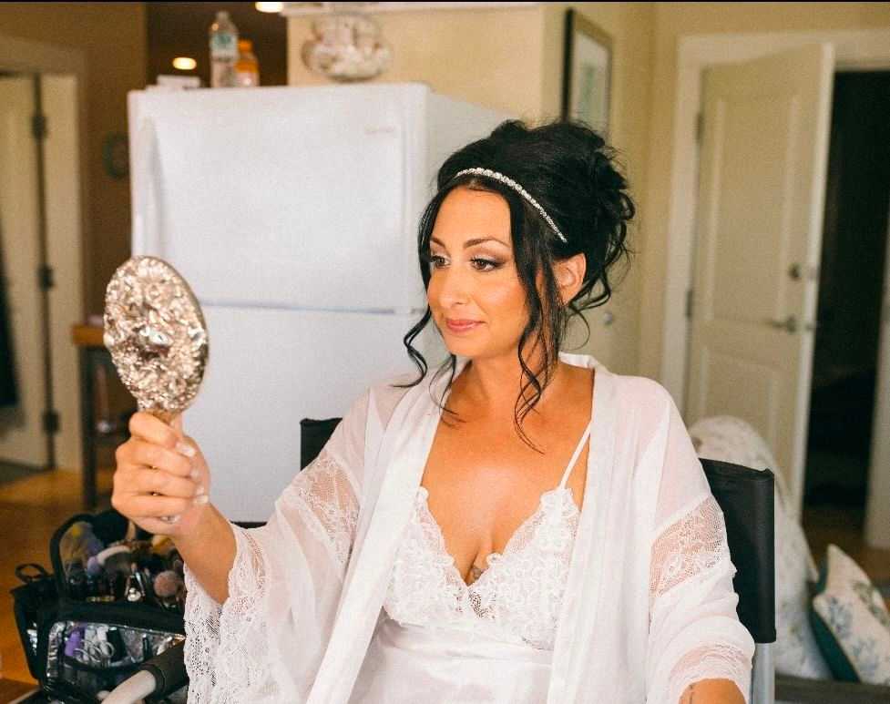Woman in a white robe looking at a handheld mirror, preparing for her wedding day.